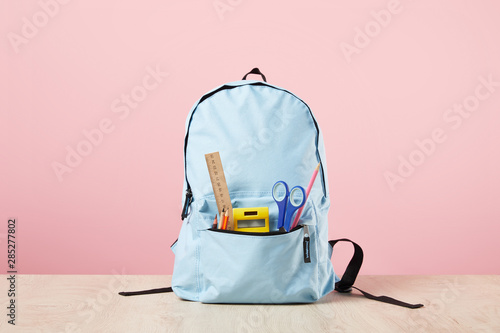 School blue backpack with stationery in pocket isolated on pink