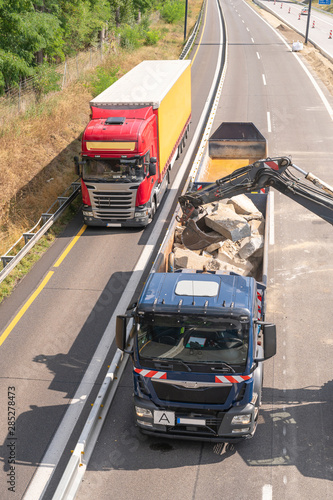 Auf einer Autobahnbaustelle wird ein LKW mit Schutt beladen und auf dem Standstreifen fährt ein LKW dicht vorbei