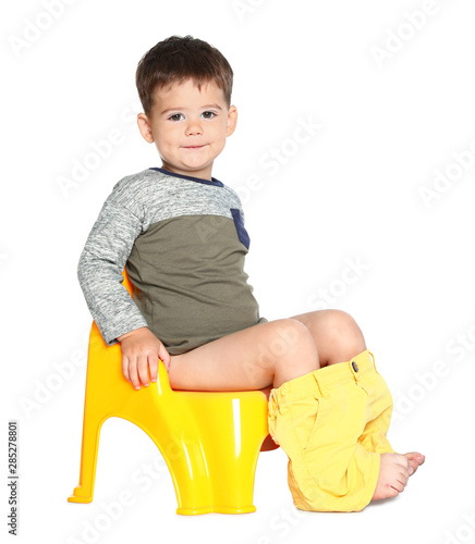 Portrait of little boy sitting on potty against white background photo