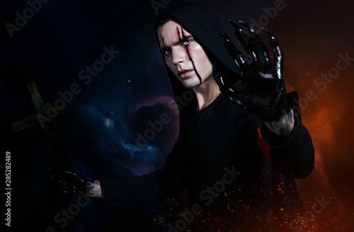 Dark fire mage in black hood with bloody scar on face holding cross with black clawed hand