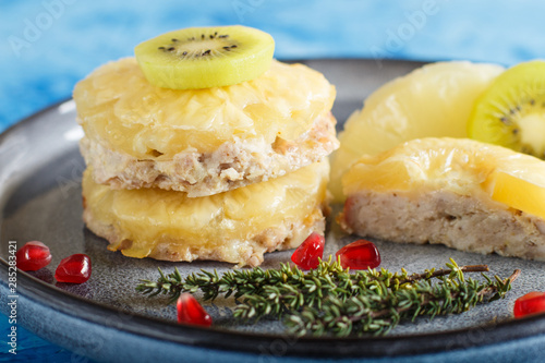 Pieces of baked pork with pineapple, cheese and kiwi on gray plate and blue background.