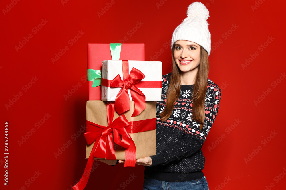 Young woman in Christmas sweater holding gift boxes on red background Young woman in Christmas sweater holding gift boxes on red background