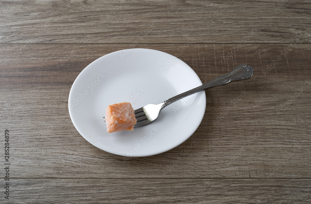 Morsel of salmon on a white plate with a fork Morsel of salmon on a white plate with a fork