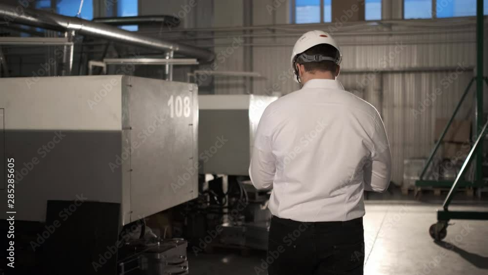 Engineer in hard hat is moving through a heavy industry factory with a tablet computer. Slow-Motion. 4k. Back View Engineer in hard hat is moving through a heavy industry factory with a tablet computer. Slow-Motion. 4k. Back View