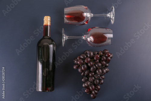 Vintage bottle of red wine without label, corkscrew & bunches of ripe organic grapes on matte blue table background. Expensive bottle of cabernet sauvignon concept. Copy space, top view, flat lay.