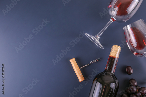 Vintage bottle of red wine without label, corkscrew & bunches of ripe organic grapes on matte blue table background. Expensive bottle of cabernet sauvignon concept. Copy space, top view, flat lay.