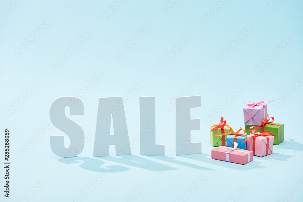 Fototapeta premium white sale lettering and festive gift boxes on blue background