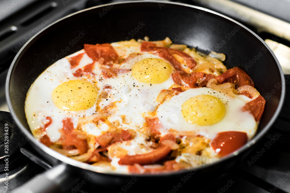 Fried eggs with onions, tomato and pepper, cooking in a pan, breakfast, healthy lifestyle