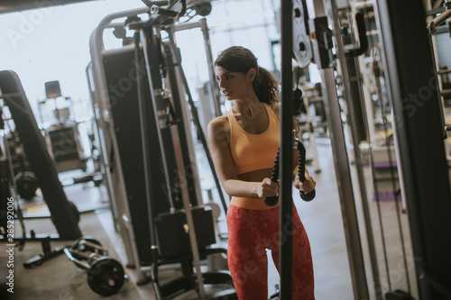 Young sporty woman working out on pull-down machine in gym