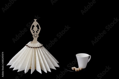 Beautiful white porcelain coffee cup with cane sugar on black saucer and stylized wooden napkin stand on black background. Minimal style. Concept - serving, restaurant, cafe, coffee, decor.