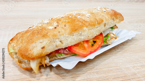 Ciabatta sandwich with lettuce, chicken and cheese on a wooden table