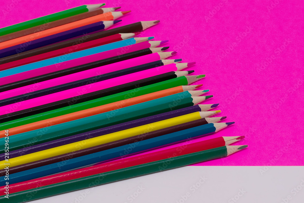 Many colored pencils lie on a white-pink background. Copy spase. The concept of back to school, the educational process, study at school, drawing Many colored pencils lie on a white-pink background. Copy spase. The concept of back to school, the educational process, study at school, drawing