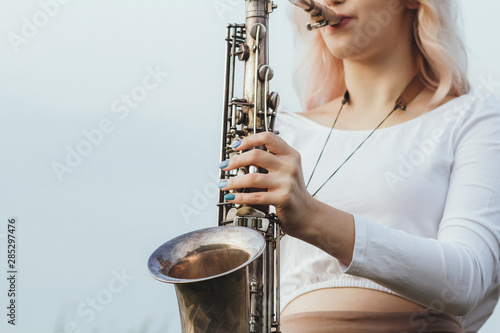 Canvas Print Portrait of young musician on nature background, woman face playing saxophone an