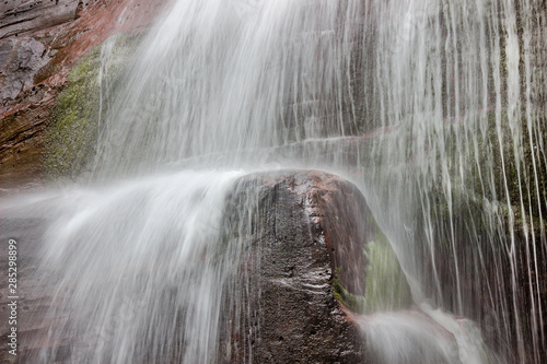 Waterfall base curtain  and blurred motion water streaming down the vertical red cliff 