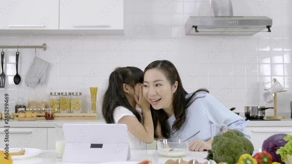 Happy Asian family little girl sharing secrets with her Mother in the kitchen at home Happy Asian family little girl sharing secrets with her Mother in the kitchen at home
