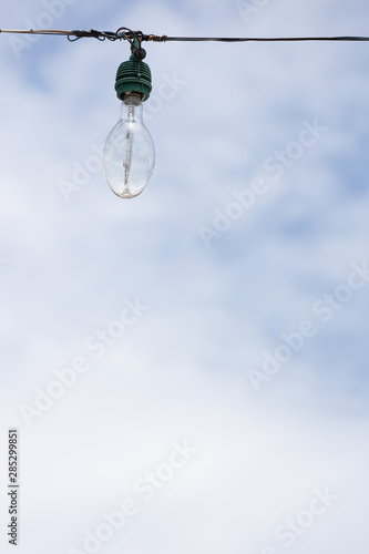 The outdoor light bulb hanging on wire with blue sky background.