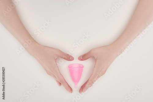 cropped view of female hands near pink plastic menstrual cup isolated on grey