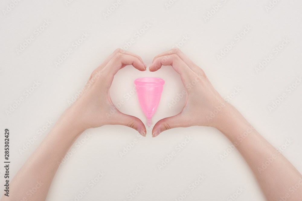cropped view of woman showing heart sign with hands around pink plastic menstrual cup isolated on grey cropped view of woman showing heart sign with hands around pink plastic menstrual cup isolated on grey