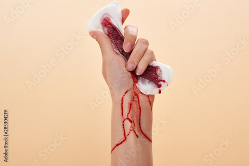 Fotografie partial view of woman squeezing sanitary towel with blood isolated on beige