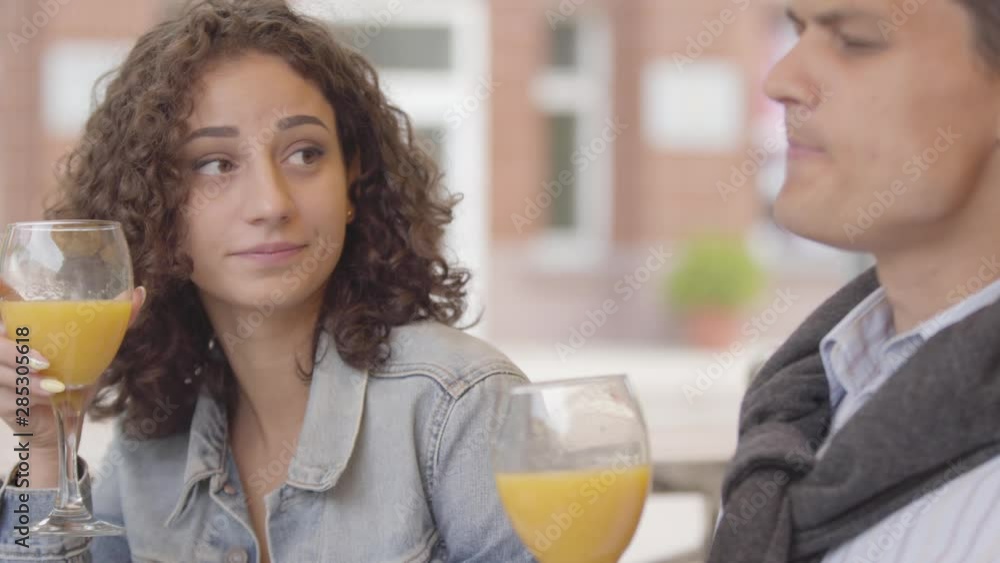 Portrait of a joyful couple chatting and laughing while drinking orange juice sitting in cafe outdoors. Young man and woman spending time together enjoying their meal. Date concept Portrait of a joyful couple chatting and laughing while drinking orange juice sitting in cafe outdoors. Young man and woman spending time together enjoying their meal. Date concept