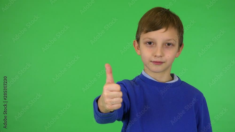 A young cute boy smiles and shows a thumb up to the camera - green screen studio A young cute boy smiles and shows a thumb up to the camera - green screen studio