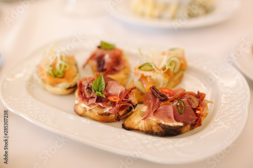 Appetizer in restaurant. Banquet concept. Bruschette with salmin and ham, decorated with basil and chile