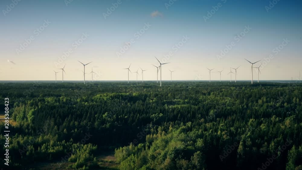 Dreamlike aerial pan of wind turbines in countryside, green treetops and blue sky, Scandinavia Dreamlike aerial pan of wind turbines in countryside, green treetops and blue sky, Scandinavia
