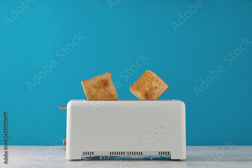 Roasted toast bread popping up of toaster with blue wall, front view