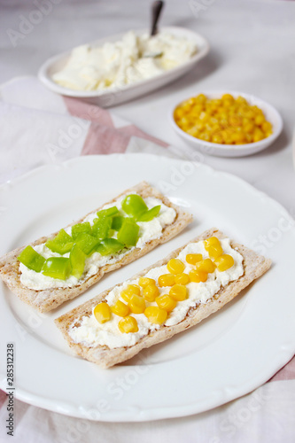 Homemade Crispbread toast with Cottage Cheese and green olives,slices of cabbage,tomatoes,corn,green pepper on cutting board on white concrete background.Healthy food concept,Top view.Flat Lay