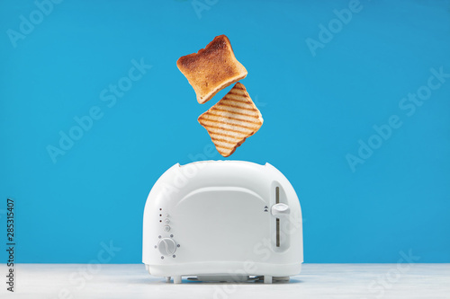 Tablou pe pânză Roasted toast bread popping up of toaster with blue wall, front view