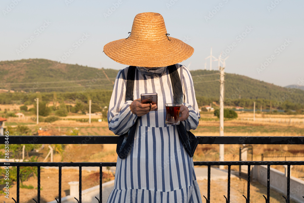 the woman wearing dress drinking tea and using mobile phone at the balcony from arid land.
