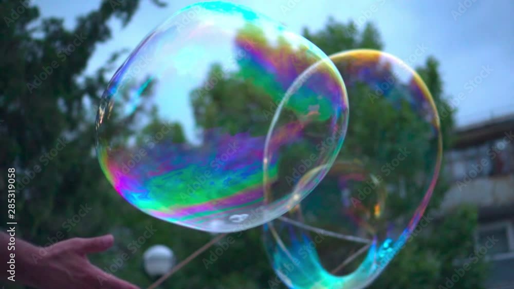 Metamorphosis of big soap Bubbles in Slow Motion. Close up view of beautiful big soap bubble is flying near the trees at sunny day. Big bubble shimmering colors of the rainbow. Metamorphosis of big soap Bubbles in Slow Motion. Close up view of beautiful big soap bubble is flying near the trees at sunny day. Big bubble shimmering colors of the rainbow.