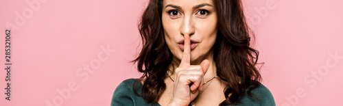 panoramic shot of attractive woman showing hush sign isolated on pink