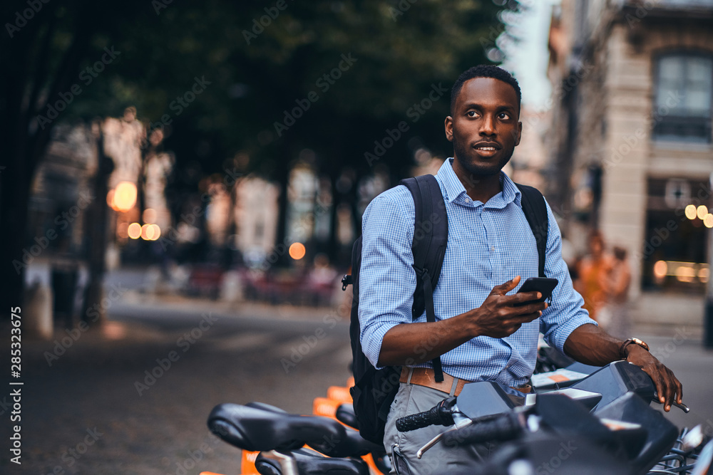 Young attractive student is renting bike and is making web payment using his mobile phone.