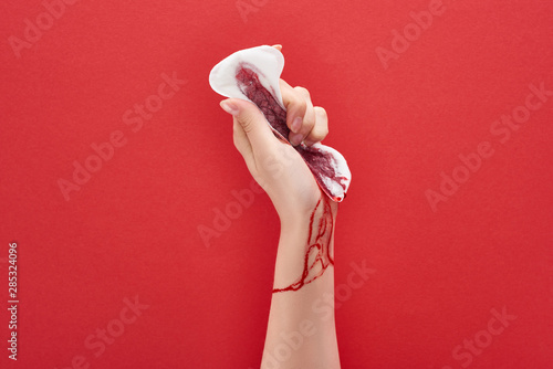 partial view of woman squeezing sanitary towel with blood on red background photo