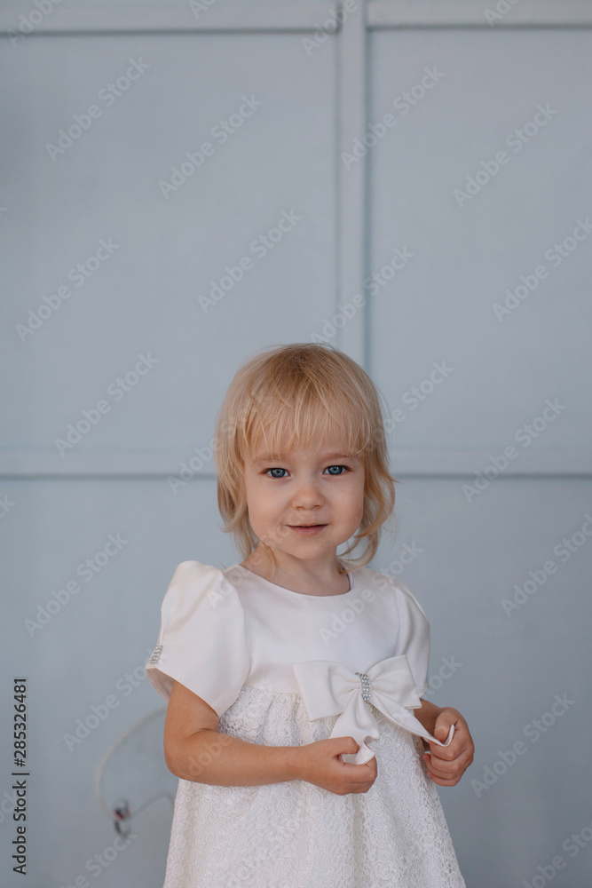 Pretty little girl in white dress by blue wall Pretty little girl in white dress by blue wall