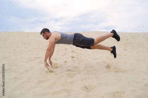 Young athletic man doing push-UPS in a jump on the sand.