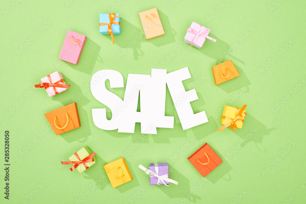 Obraz premium round frame of decorative gift boxes and shopping bags on green background with sale lettering