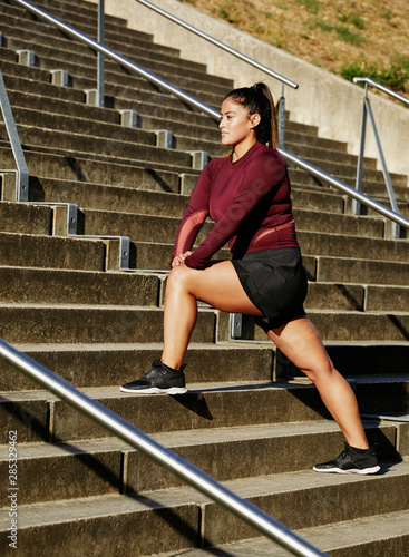 Body confident woman stretching legs on strairs after a workout outdoors photo