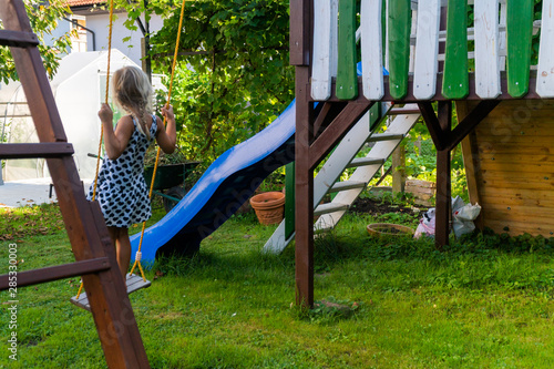 3-5 year old blond girl having fun on a swing outdoor. Summer playground. Girl swinging high. Young child on swing in garden
