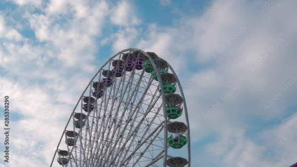 Ferris wheel rotates on the background of passing clouds in the blue sky. children's amusement ferris wheel sunny summer day. Ferris wheel rotates on the background of passing clouds in the blue sky. children's amusement ferris wheel sunny summer day.