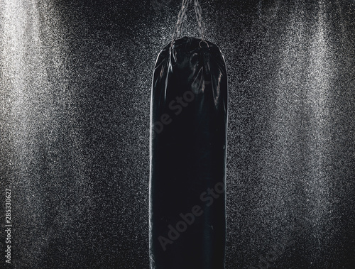 Fotografie Black leather punching bag in dark room with light water splashes
