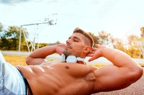 Fotografie Muscular fitness handsome man doing sit ups outdoor in a sport park