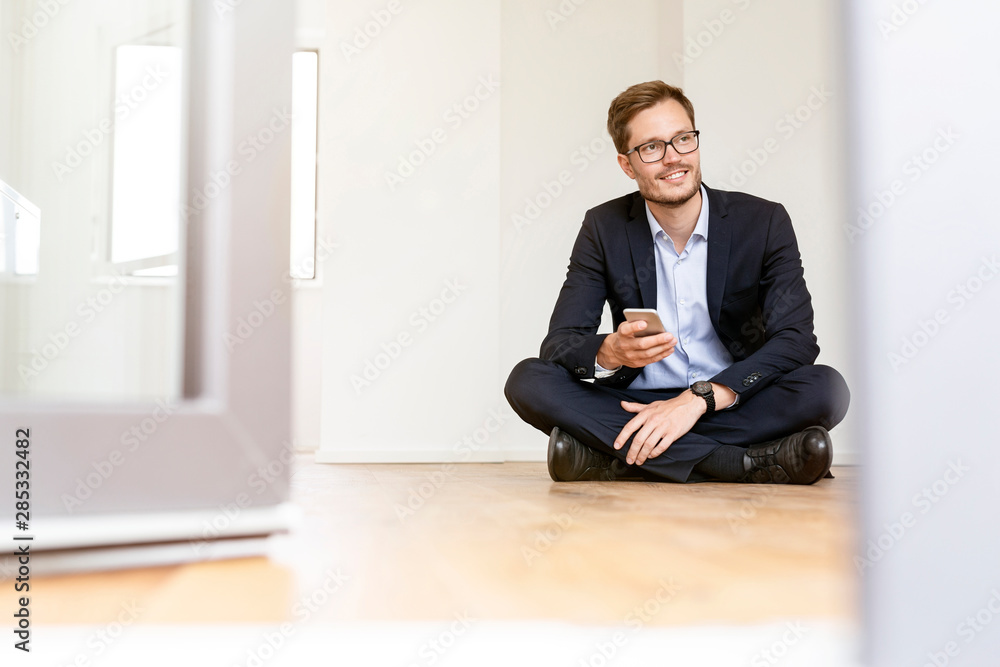 Smiling businessman sitting on the floor with cell phone Smiling businessman sitting on the floor with cell phone