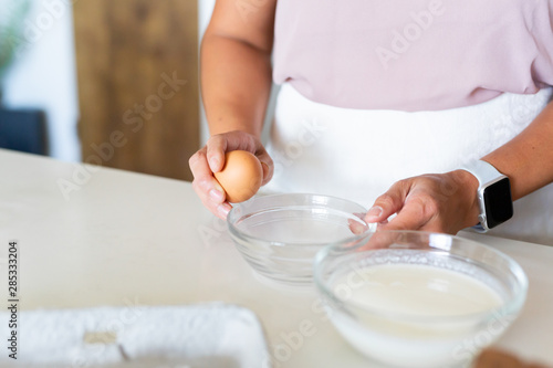 woman cracking egg open over glass bowl