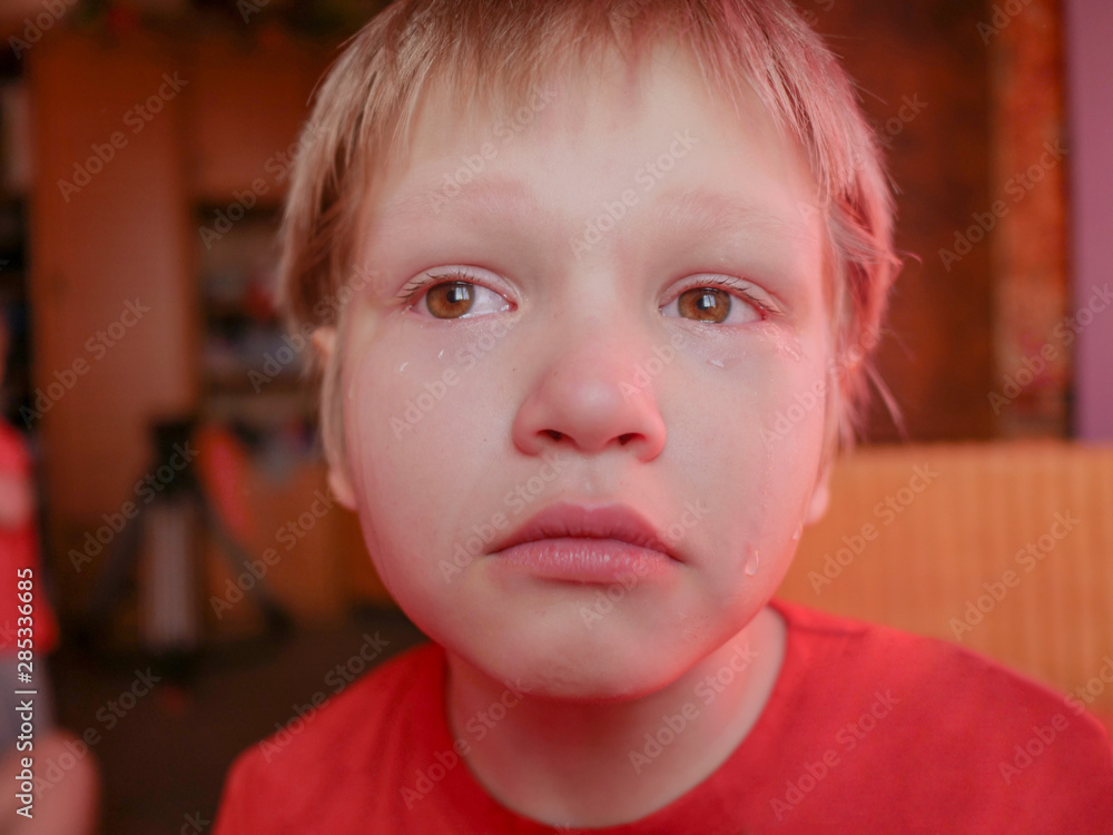 Upset child in red sweater on red background is crying and actively expresses emotions. Close up little kid boy in glasses crying with tearful on her face Upset child in red sweater on red background is crying and actively expresses emotions. Close up little kid boy in glasses crying with tearful on her face