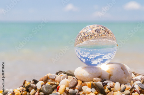 Glass round ball on the beach reflects the sea in summer