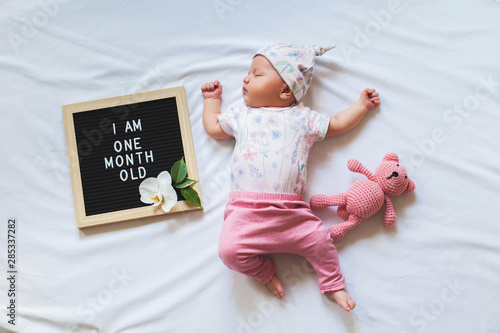 Принти на полотні Cute one month old baby girl in trendy outfit laying between letter board and teddy bear