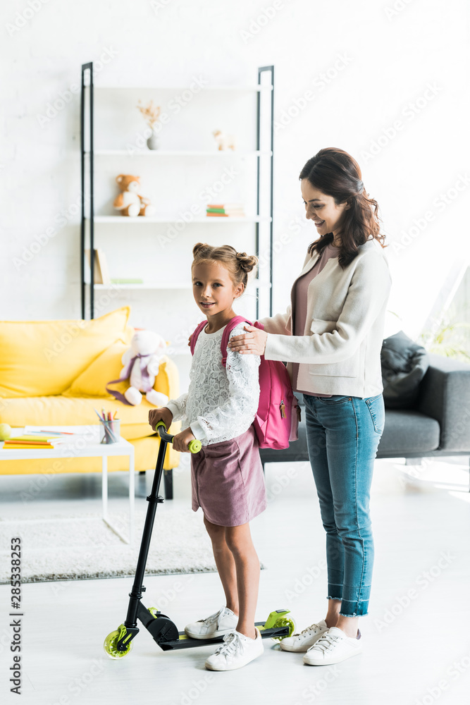 attractive mother standing with cute daughter and kick scooter