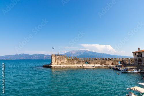 NAFPAKTOS / GREECE - JUNE 27, 2019: View of the port of Nafpaktos with the famous statue and a greek flag